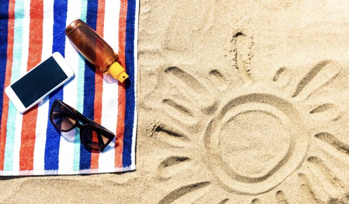 Handdoek op het strand met een telefoon, zonnebril en zonnebrand. In het zand is een zon getekend