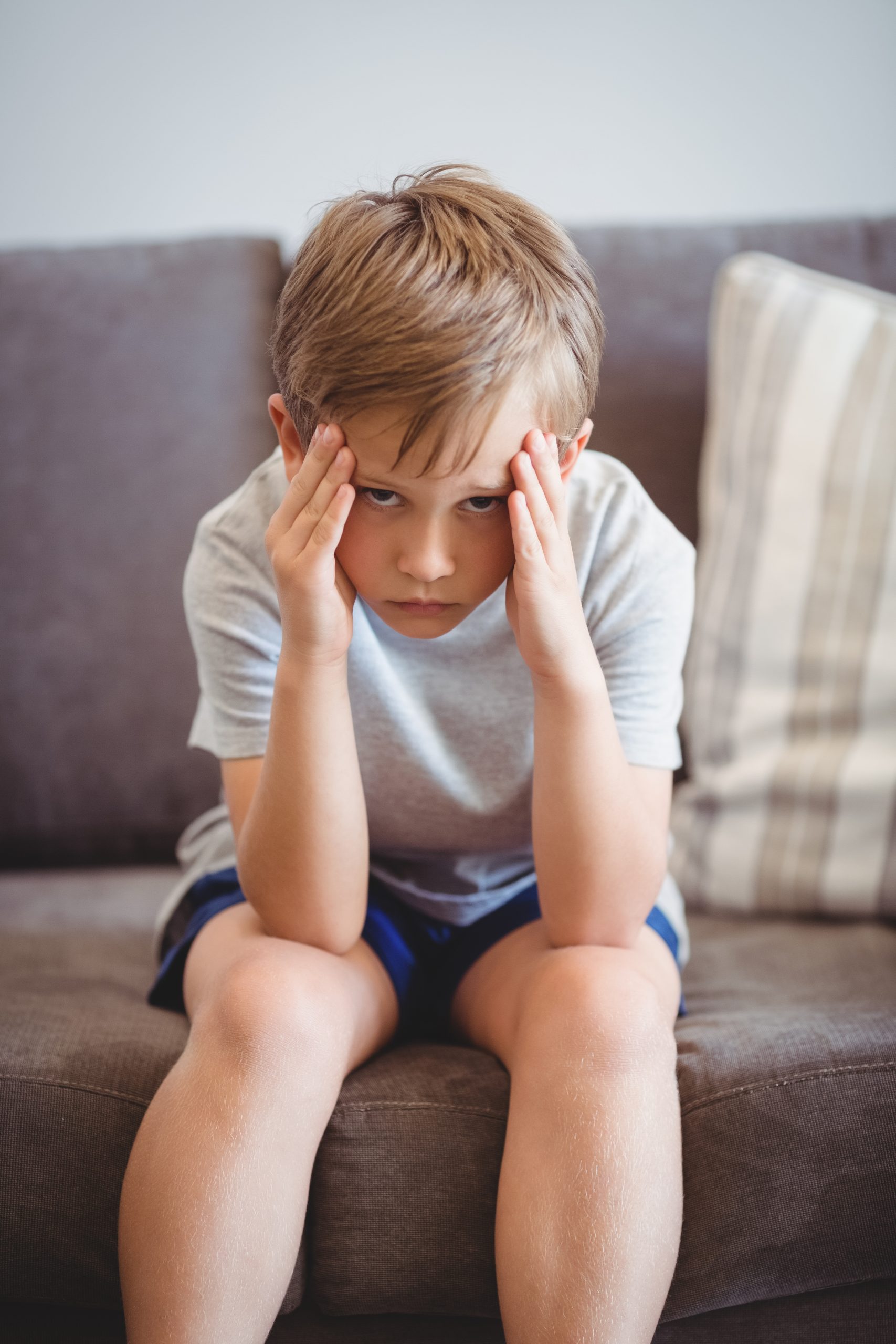 Boze jongen zit op de bank met zijn handen tegen zijn hoofd, zichtbaar gefrustreerd