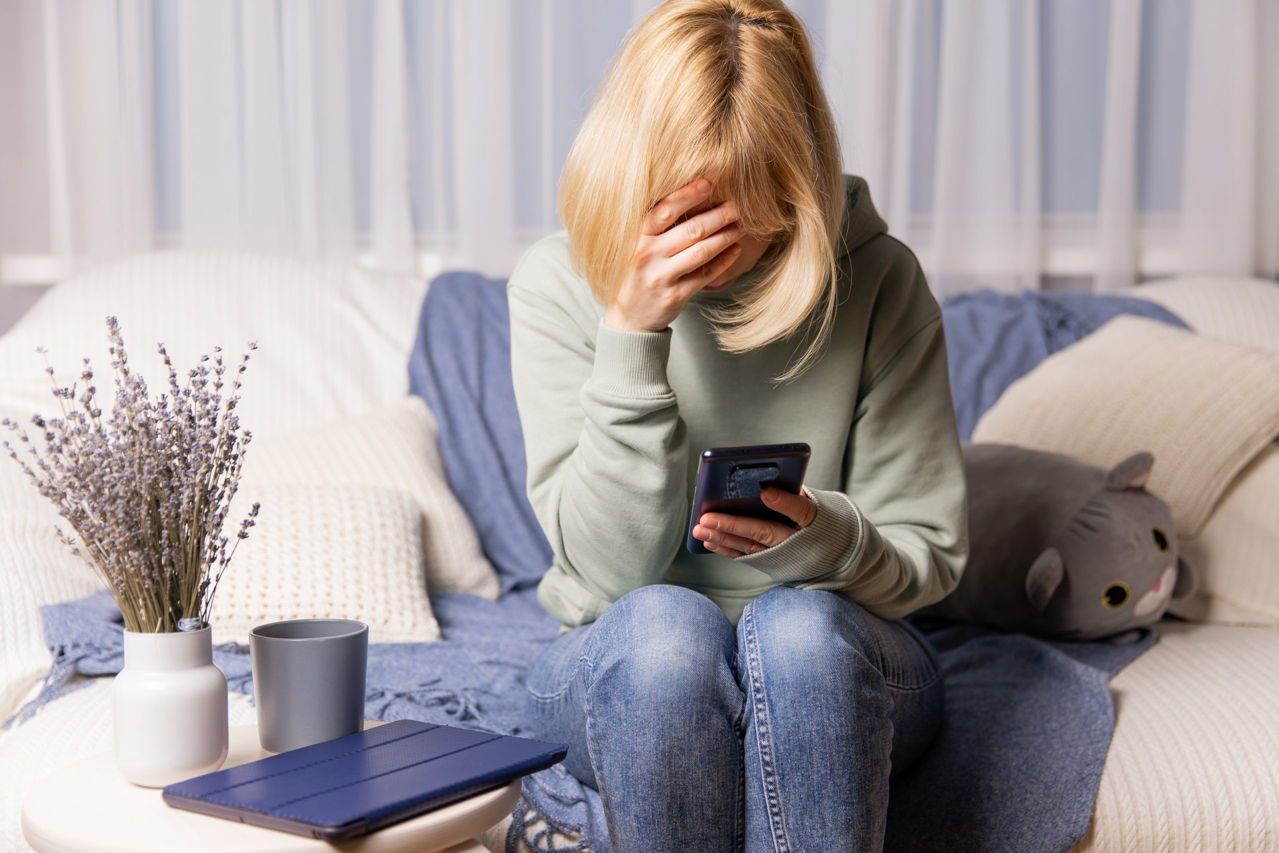 Bezorgde vrouw kijkt naar haar smartphone, mogelijk geconfronteerd met online afpersing of financiële sextortion.