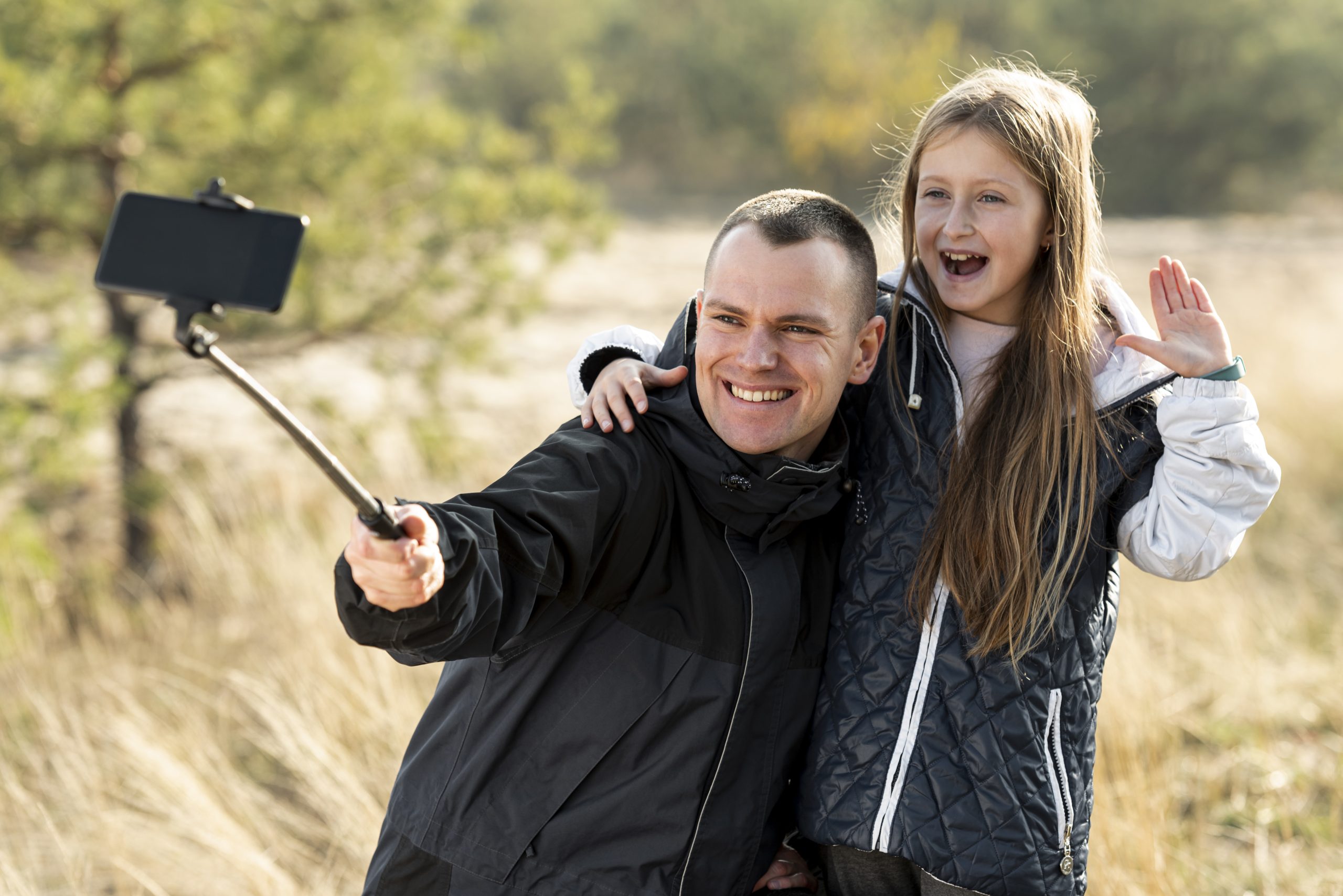 Vader en dochter maken samen een vrolijke vlog met een selfiestick in de natuur.