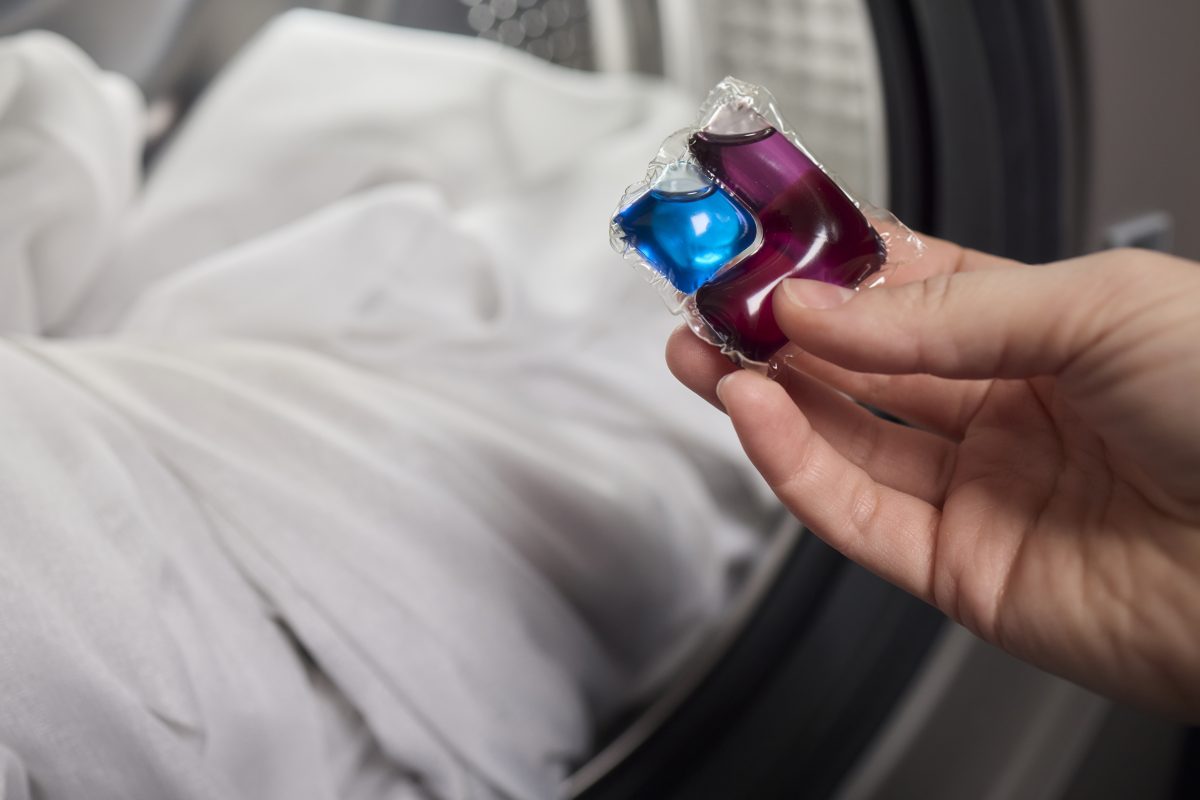 Hand met wascapsule voor een open wasmachine