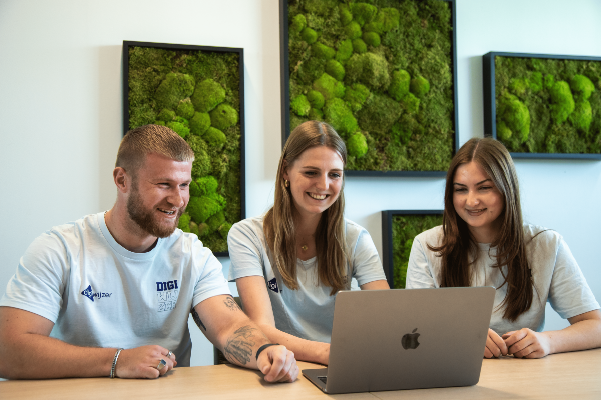 Drie medewerkers van Digiwijzer kijken lachend naar een laptop tijdens een overleg over digitale toegankelijkheid voor scholen.