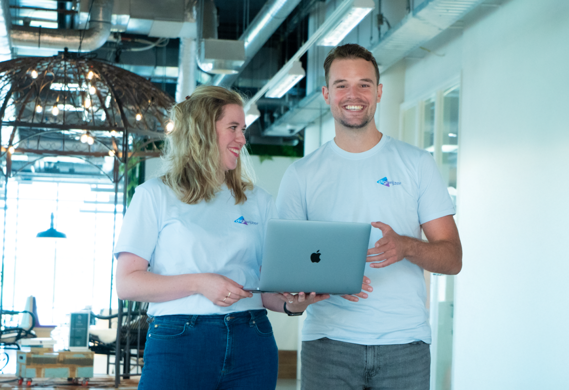 Twee teamleden van Digiwijzer staan lachend met een laptop in een moderne kantoorruimte.