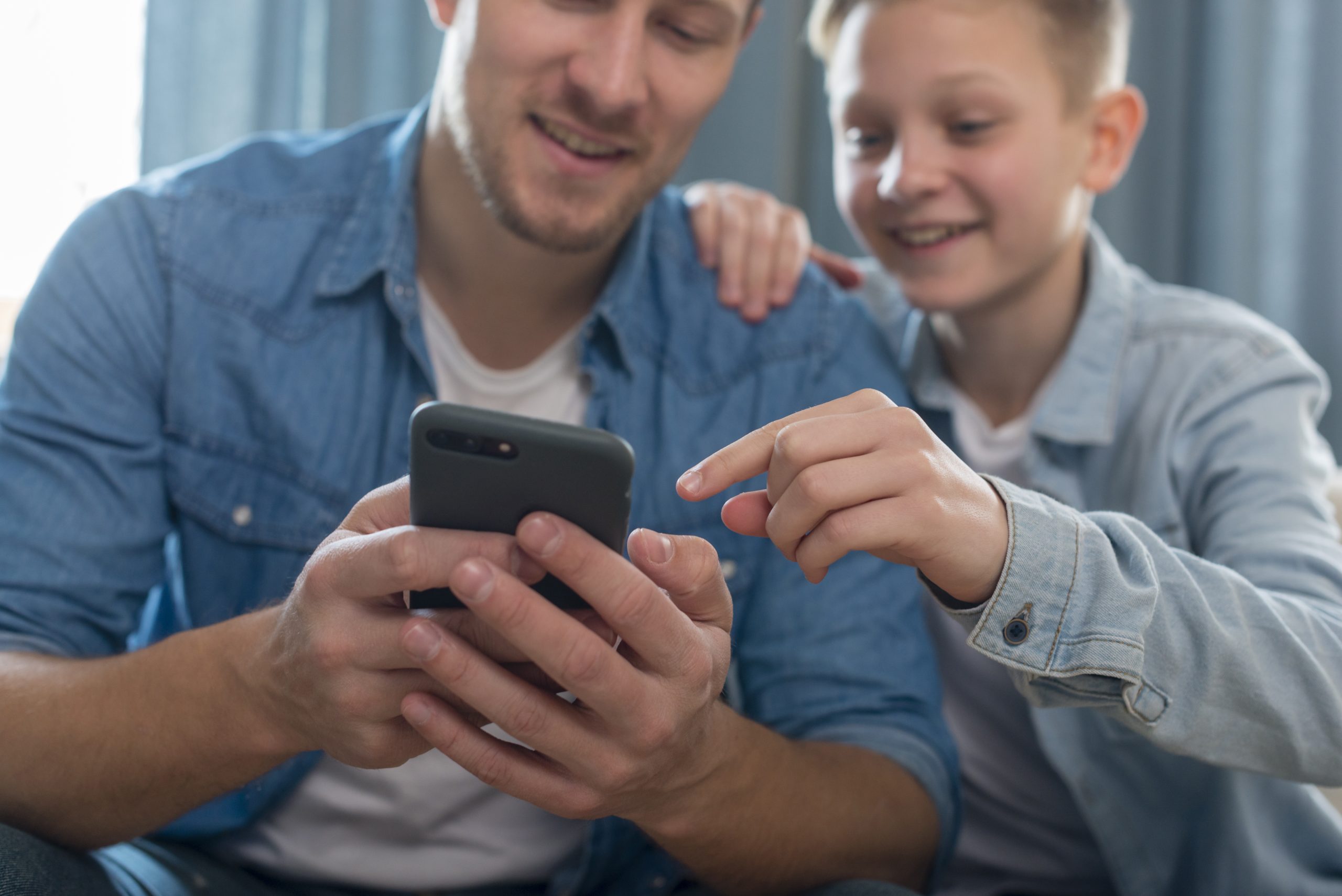 Vader en zoon kijken samen naar een smartphone en bespreken wat er op het scherm gebeurt