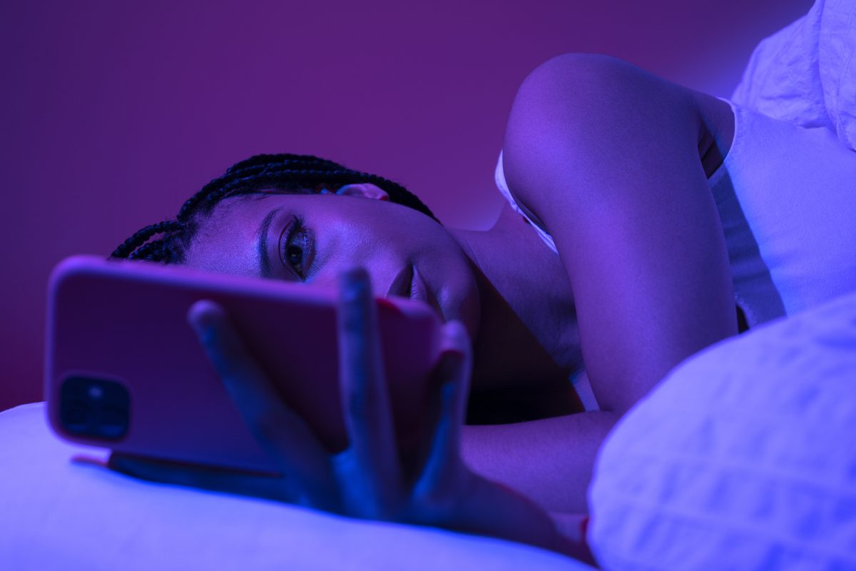 Tienermeisje kijkt in bed op haar smartphone bij paarsblauw licht