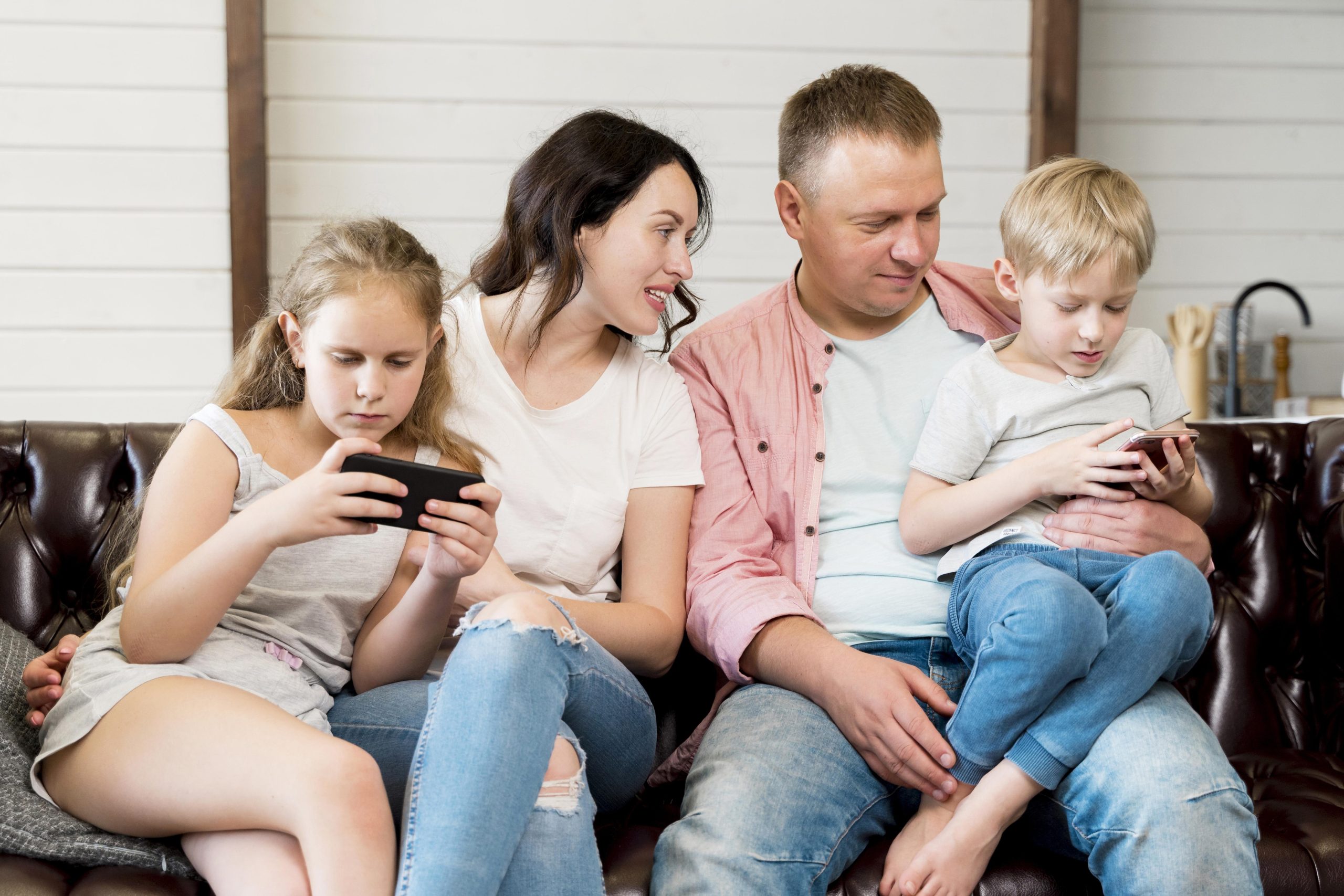 Ouders zitten op de bank en begeleiden hun kinderen die op smartphones kijken