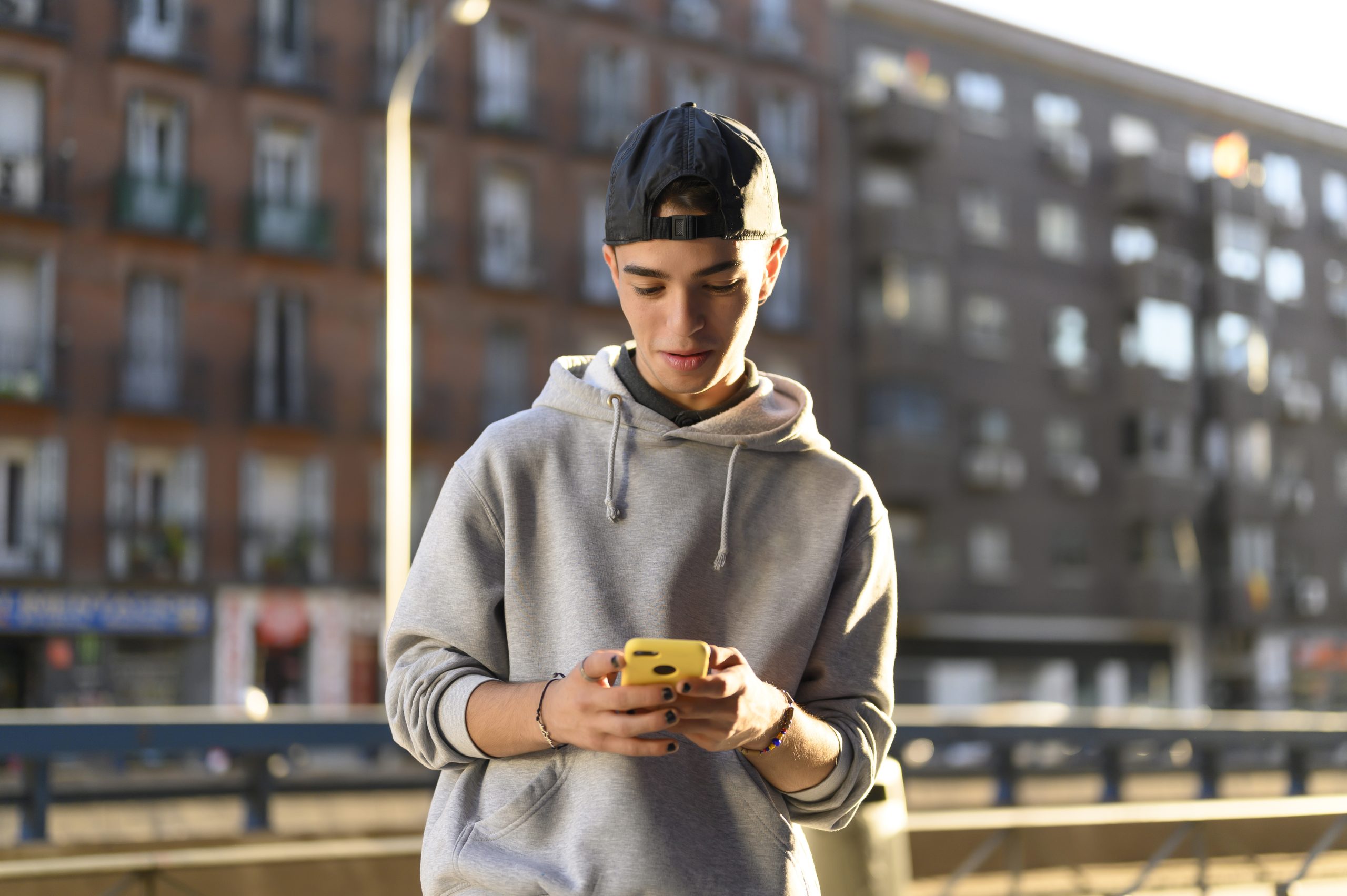 jongere kijkt glimlachend op zijn smartphone terwijl hij buiten staat, mogelijk in gesprek met een AI-chatbot