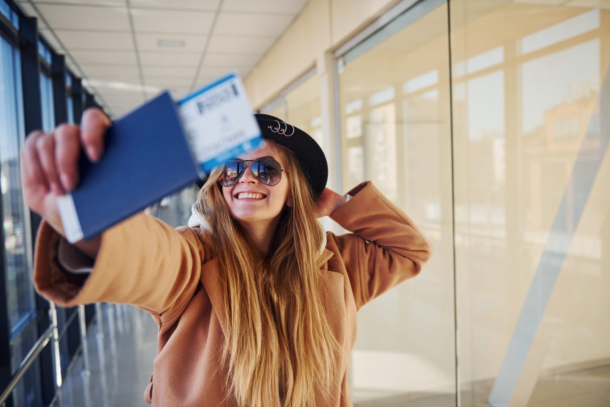 Jonge vrouw op het vliegveld maakt selfie met boardingpass en paspoort zichtbaar