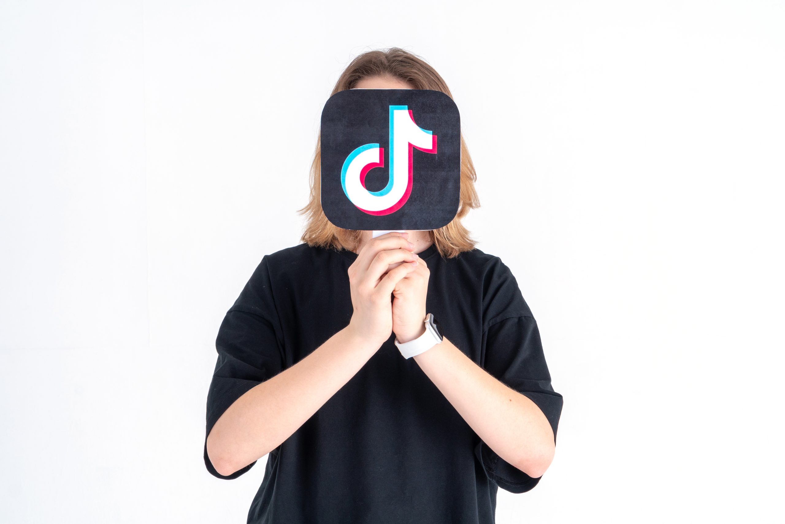 Tiener houdt TikTok-logo voor zijn gezicht tegen een witte achtergrond.