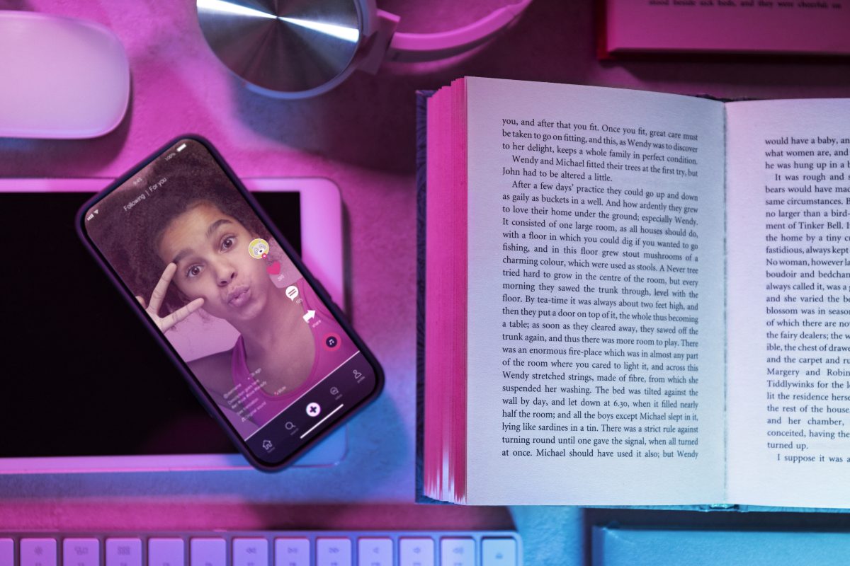 Smartphone met TikTok-video op de For You Page naast een open boek, symbool voor de keuze tussen online en offline media.