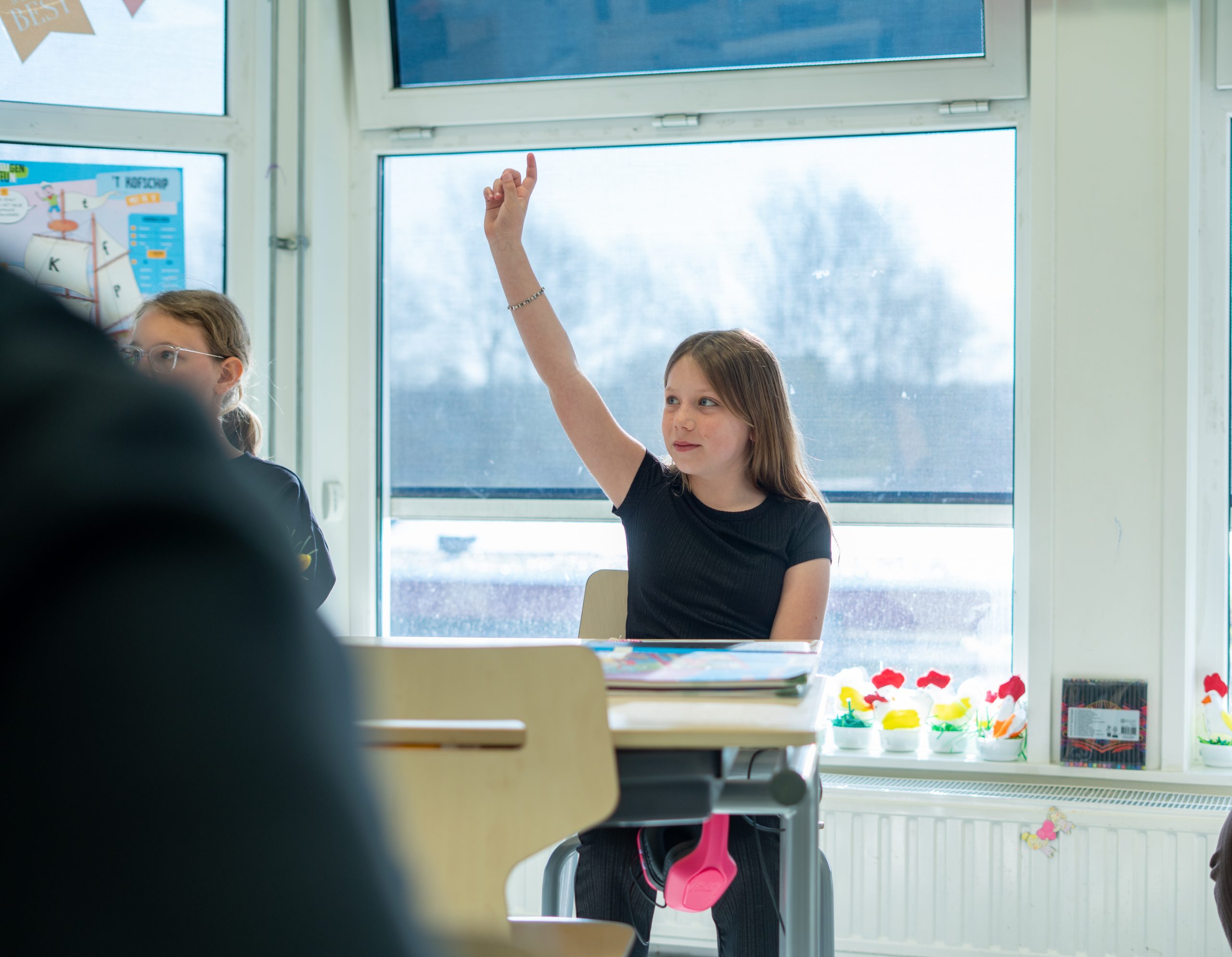 Leerling steekt enthousiast haar hand op tijdens een interactieve les in de klas.