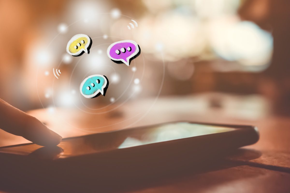 Vinger die een smartphone aanraakt met kleurrijke chatballonnen die boven het scherm zweven, symbool voor online interactie.