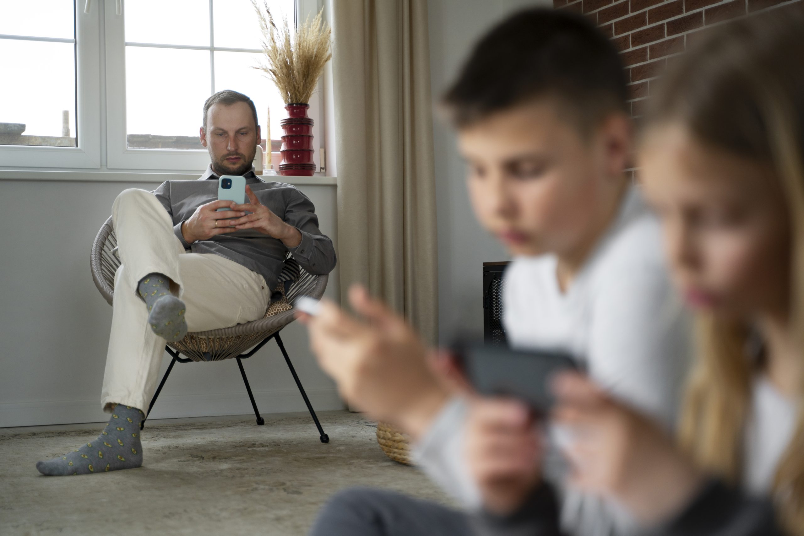 Vader houdt toezicht terwijl twee kinderen op hun smartphones spelen in de woonkamer.