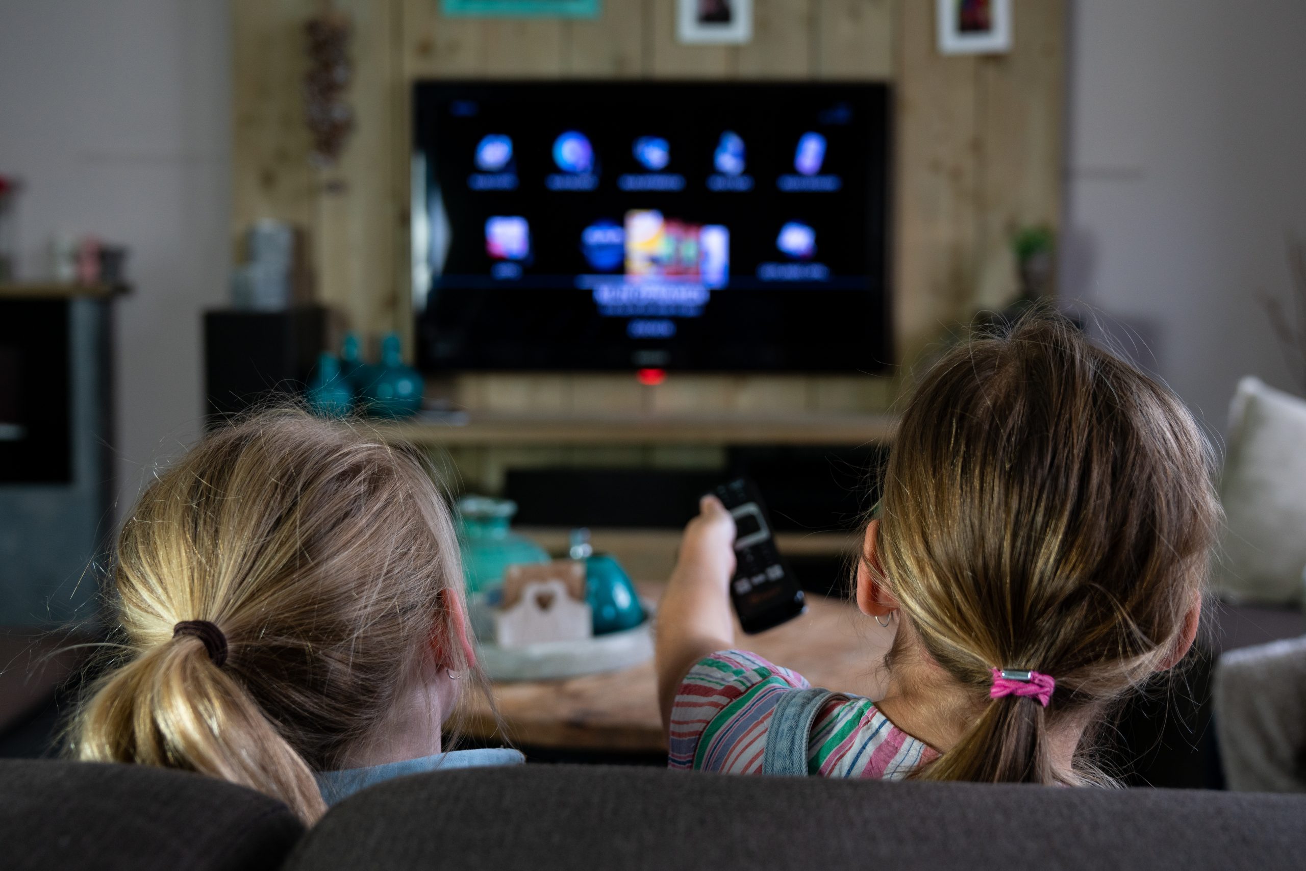 Twee jonge kinderen zitten samen op de bank en kijken televisie in de woonkamer.