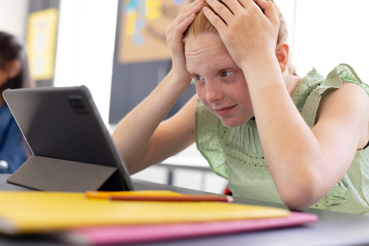 Leerling kijkt gefrustreerd naar een tablet tijdens de les.