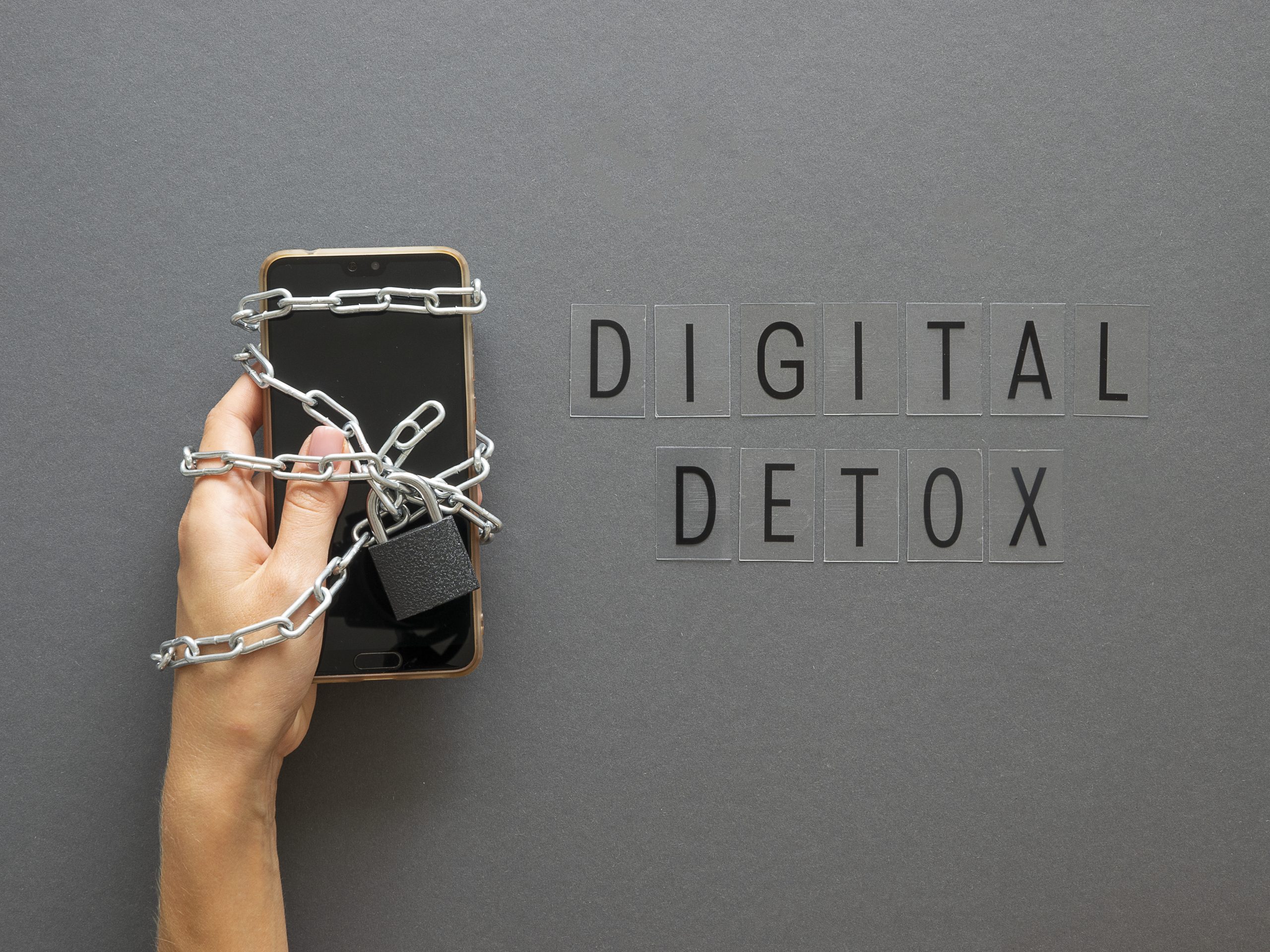 Hand die een smartphone vasthoudt, omwikkeld met een metalen ketting en hangslot, naast de woorden “Digital Detox”.