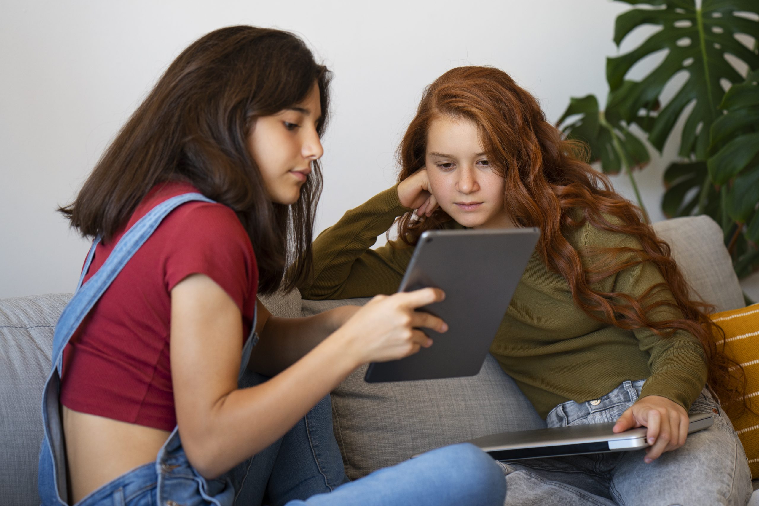 Twee meisjes zitten samen op een bank en kijken geconcentreerd naar een tablet.
