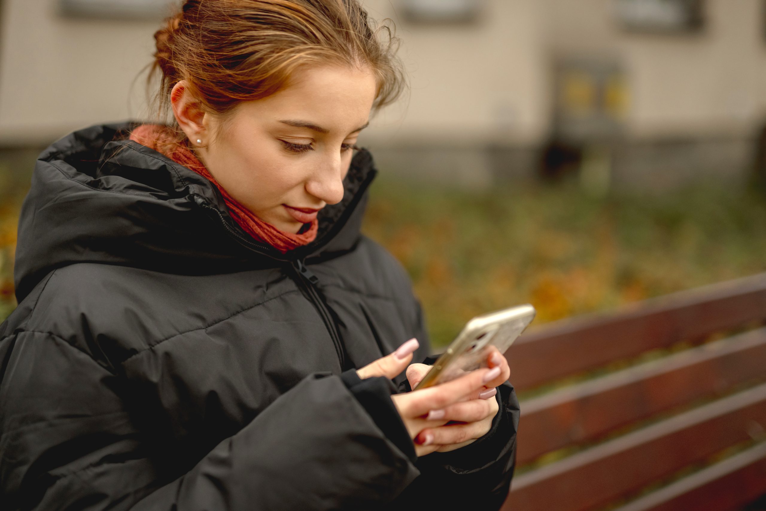 Jongere kijkt geconcentreerd op smartphone terwijl zij buiten op een bankje zit