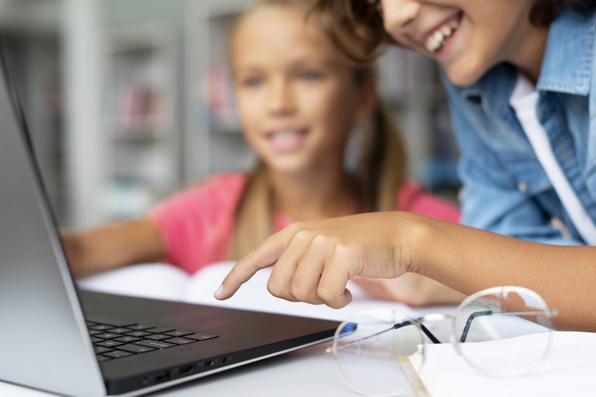 Twee leerlingen werken samen aan schoolwerk op een laptop in een leeromgeving.