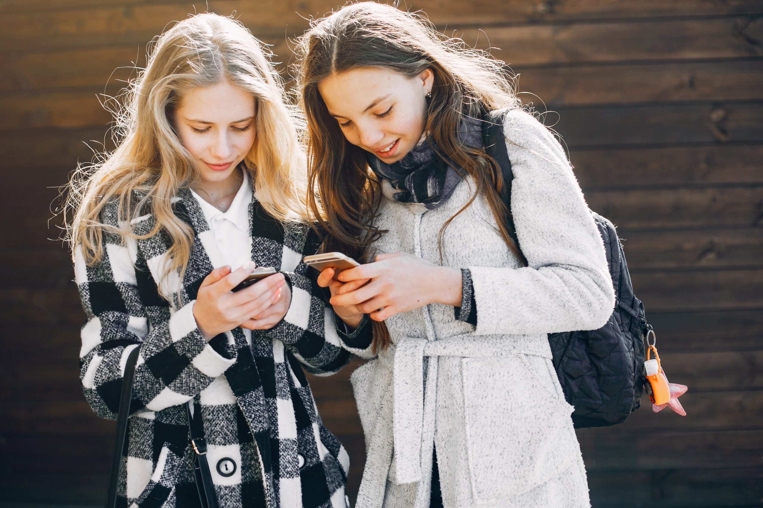 Twee pubermeiden kijken samen op hun smartphone en lachen terwijl ze buiten staan.