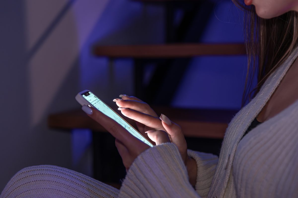 Jongere zit βs avonds op een trap en scrollt op haar smartphone in het donker.