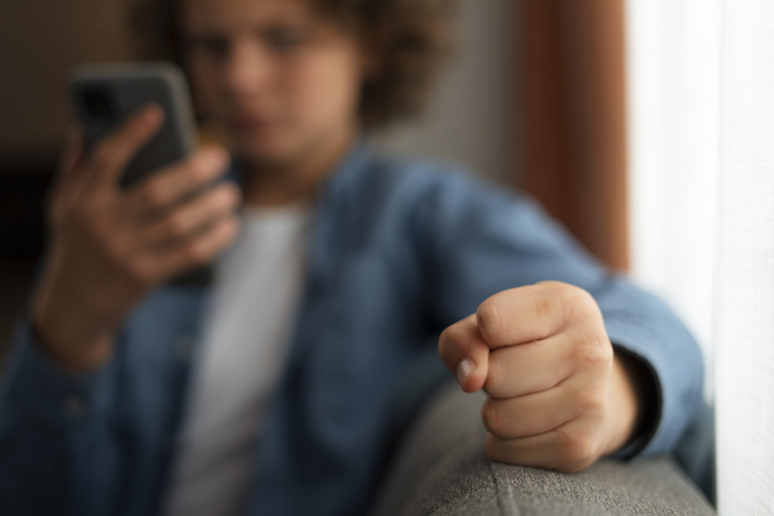 Jongere kijkt boos en gefrustreerd naar zijn telefoon terwijl hij een gebalde vuist maakt, passend bij afwijzing en negatieve online ervaringen