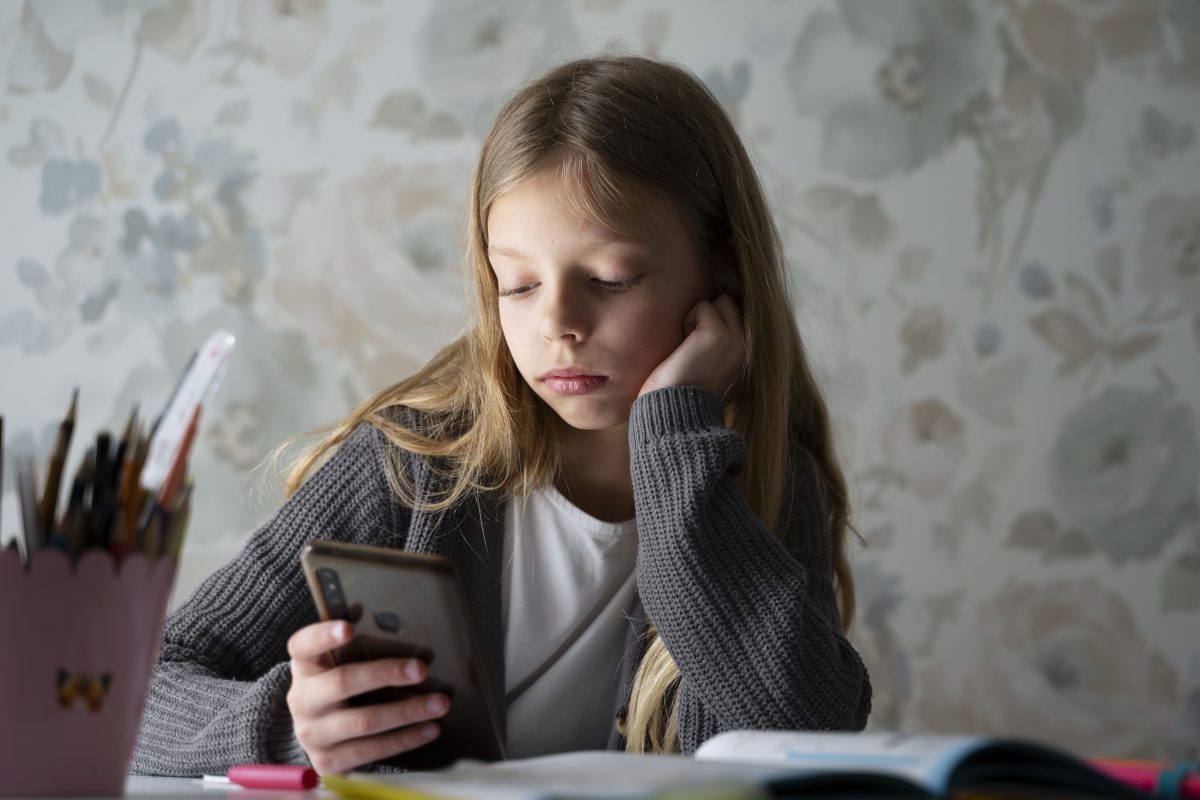 Meisje kijkt bezorgd naar haar smartphone tijdens het maken van huiswerk, passend bij online pesten en sociale media bij jongeren.