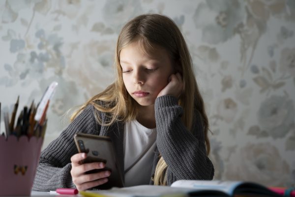 Meisje kijkt bezorgd naar haar smartphone tijdens het maken van huiswerk, passend bij online pesten en sociale media bij jongeren.