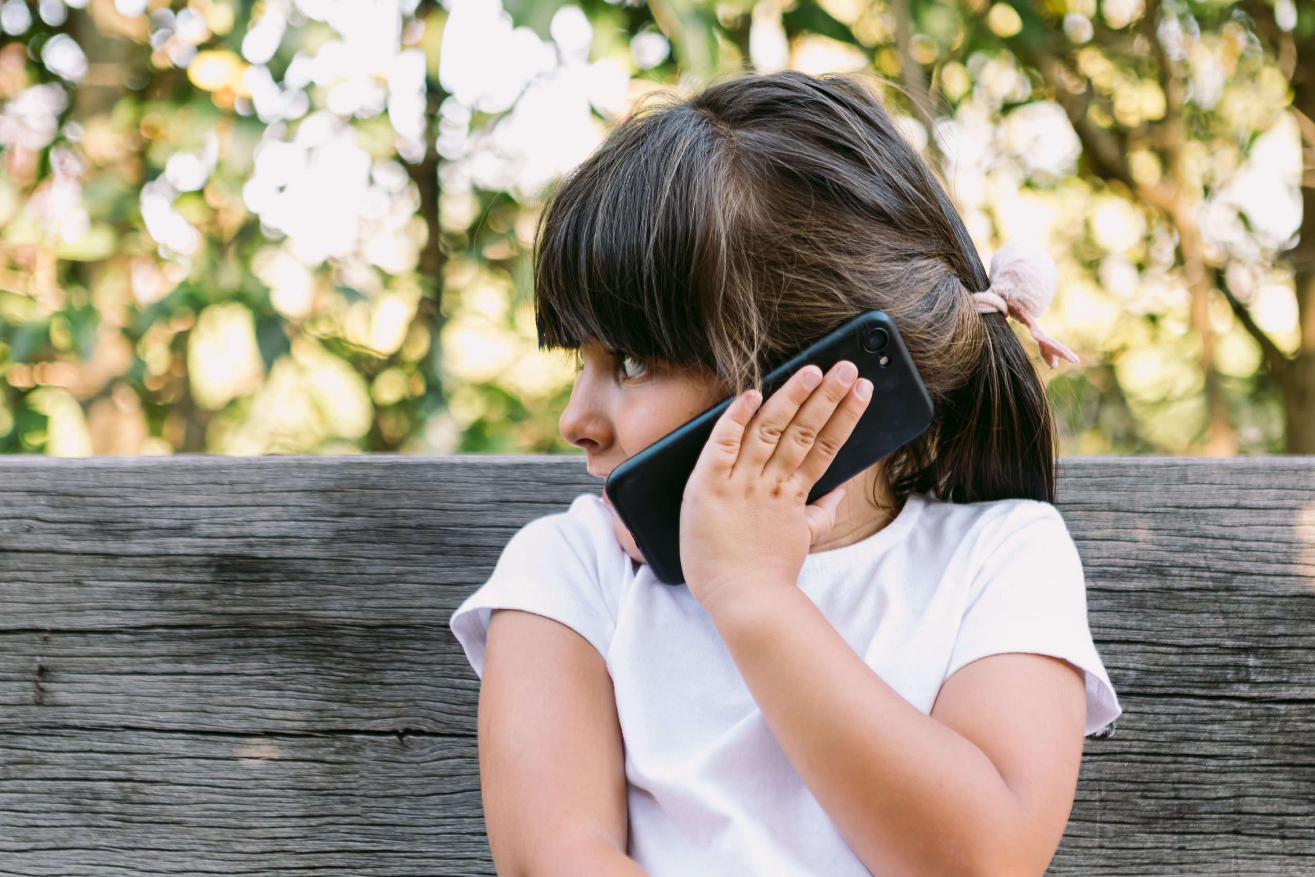 jong meisje met telefoon tegen oor op bankje dat belangst bij jongeren laat zien