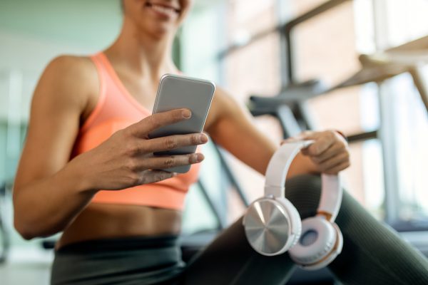 Jongere sporter gebruikt smartphone en koptelefoon in de sportschool terwijl ze muziek streamt tijdens een workout via Spotify.