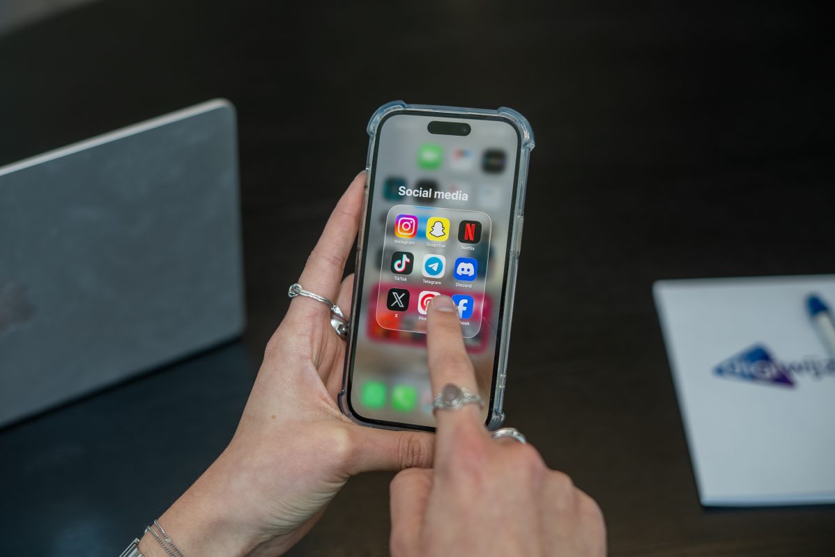 Persoon houdt een smartphone vast met een map vol socialmedia-apps zoals Instagram, TikTok, Snapchat en Discord in beeld.