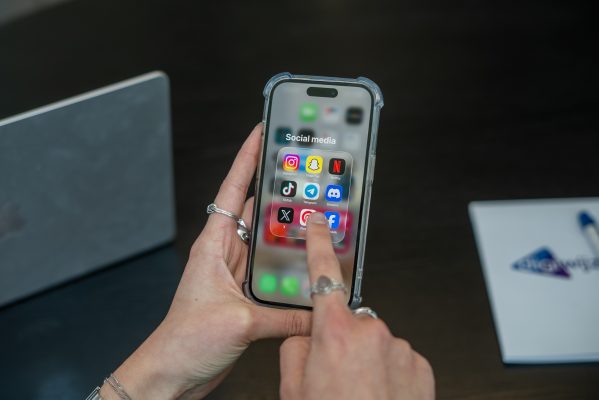 Persoon houdt een smartphone vast met een map vol socialmedia-apps zoals Instagram, TikTok, Snapchat en Discord in beeld.