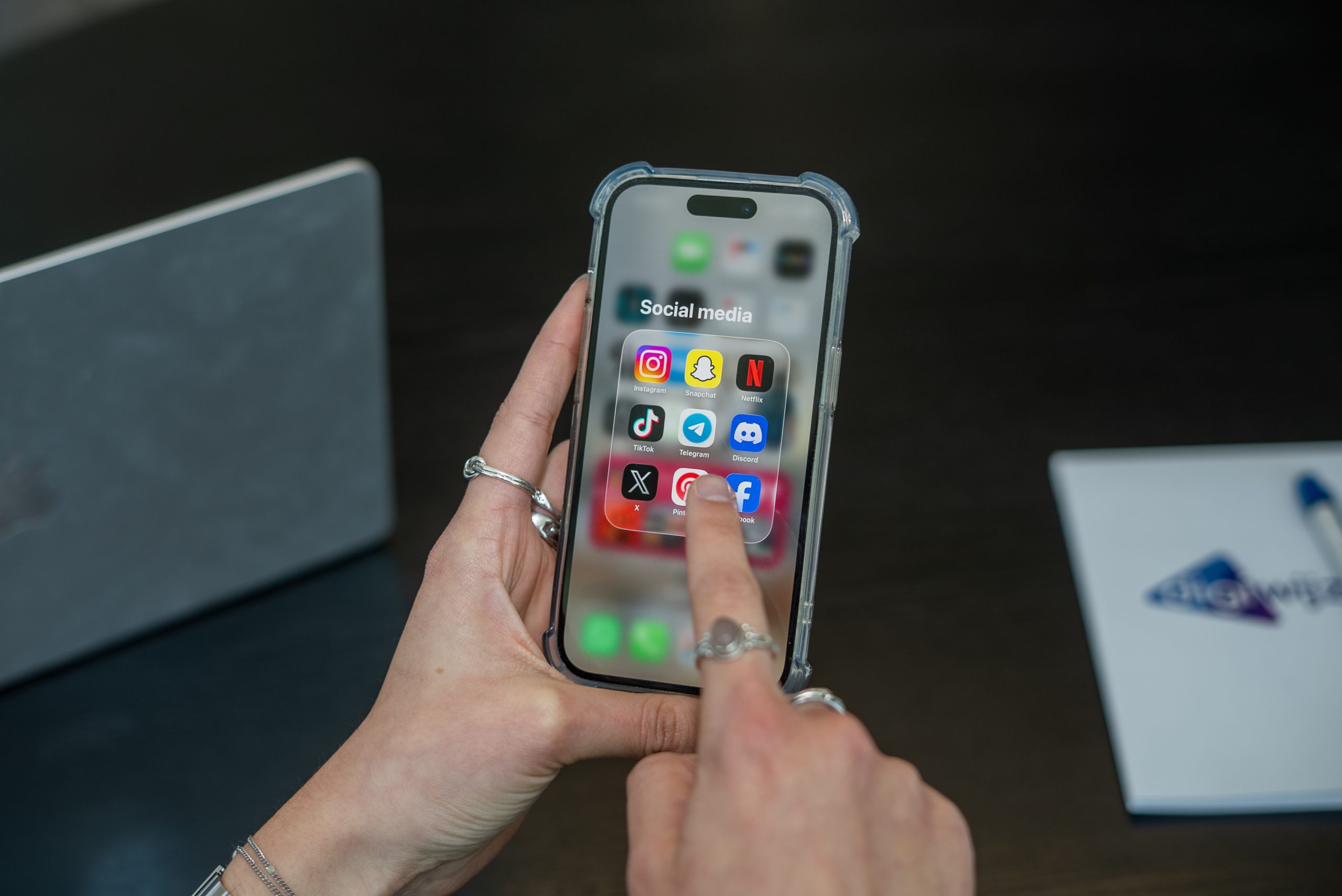 Persoon houdt een smartphone vast met een map vol socialmedia-apps zoals Instagram, TikTok, Snapchat en Discord in beeld.