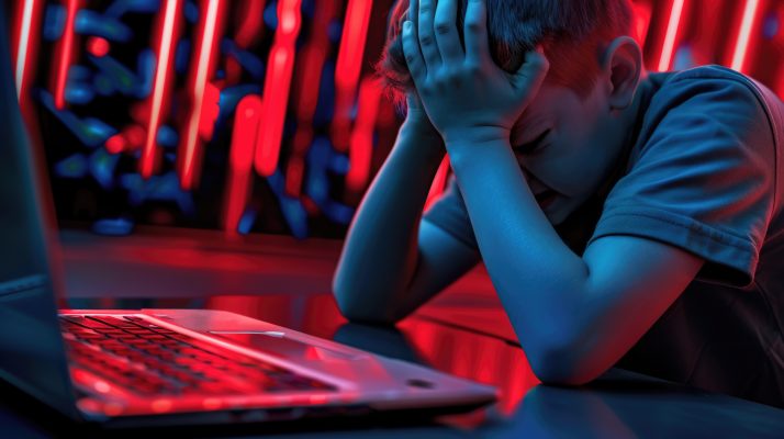 Jongen zit zichtbaar verdrietig achter een laptop terwijl hij mogelijk te maken heeft met cyberpesten en online pesten.