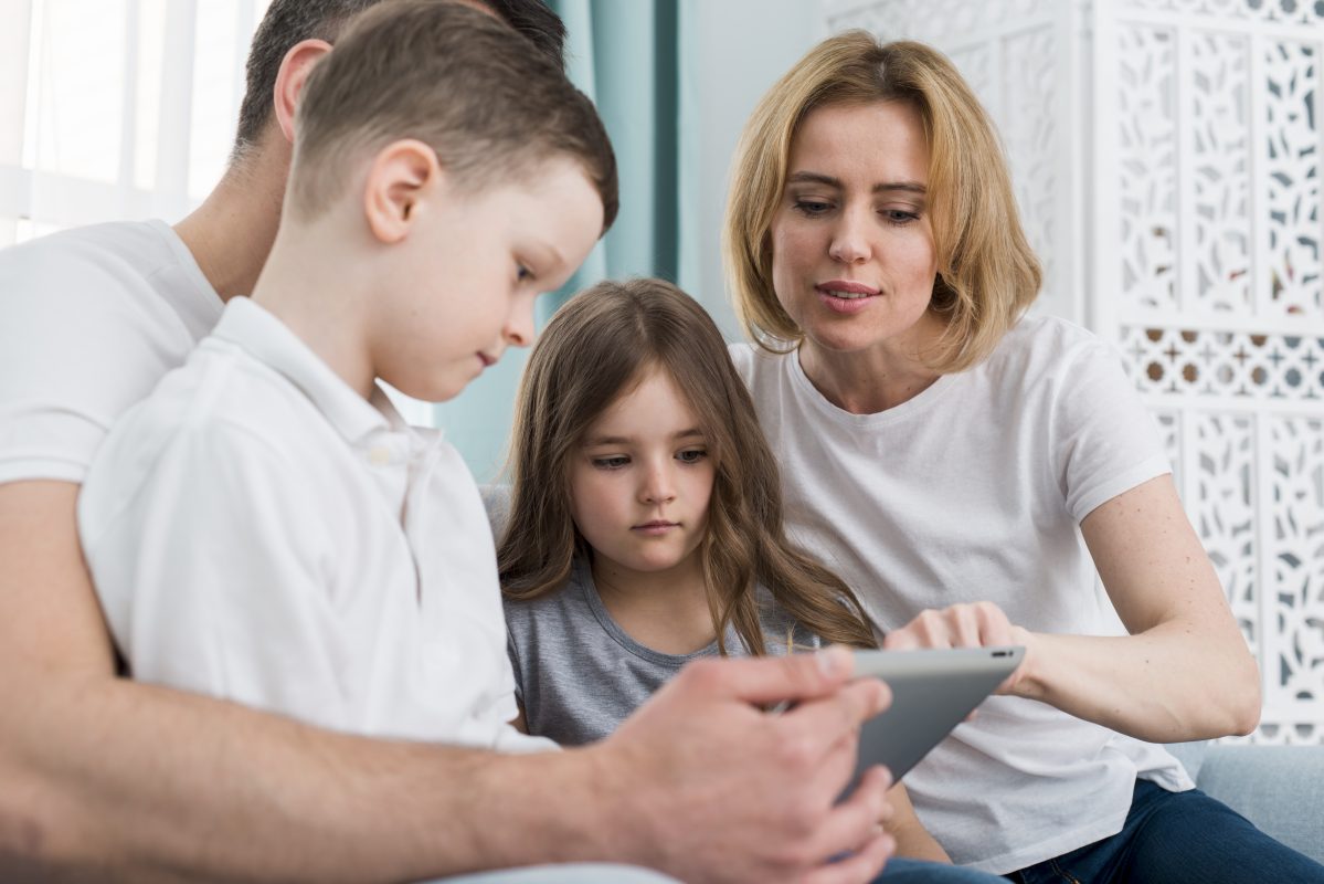 Ouders begeleiden hun kinderen bij het gebruik van een tablet thuis en bespreken samen digitale instellingen en online veiligheid.