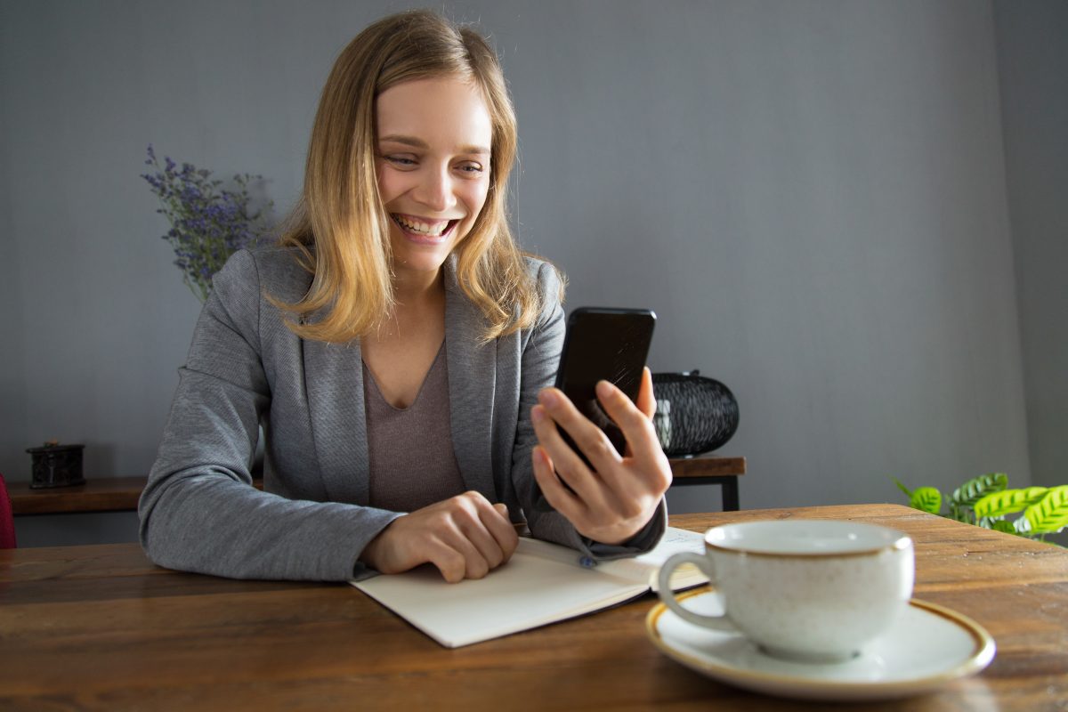 Jonge vrouw bekijkt glimlachend een bericht op haar smartphone, passend bij het thema solliciteren via social media en digitaal contact met werkgevers.