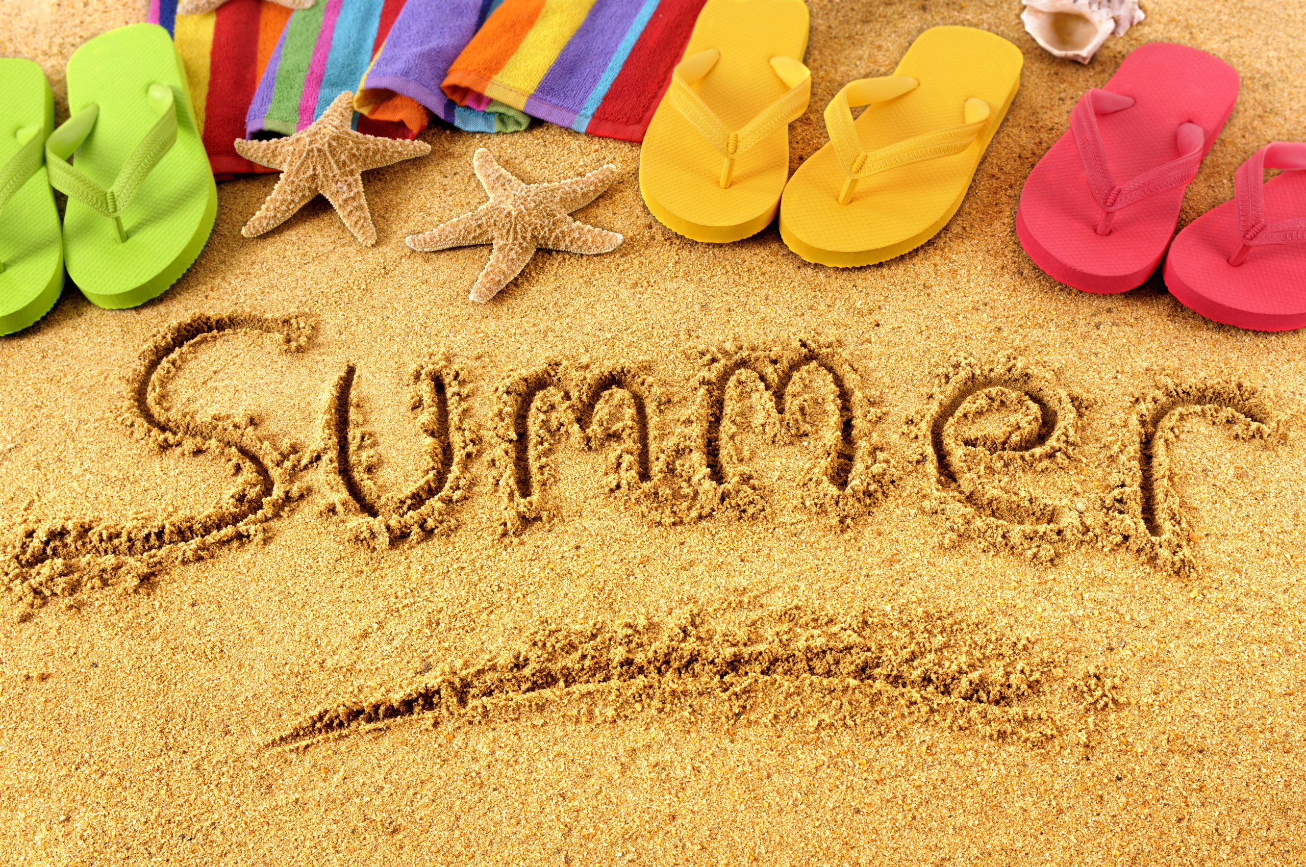 Zomerse strandafbeelding met kleurrijke handdoeken, slippers, zeesterren en het woord 'Summer' geschreven in het zand.