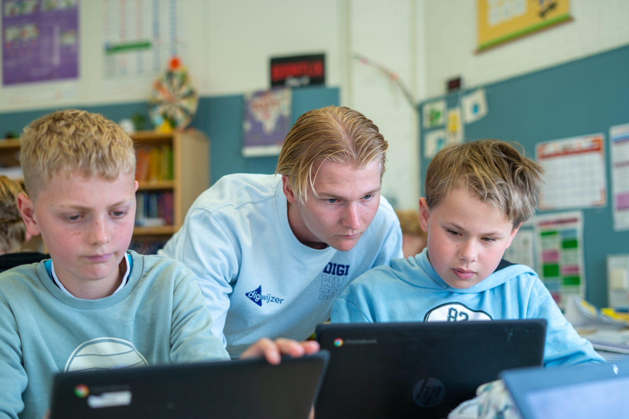Een Digiwijzer-digicoach helpt twee leerlingen tijdens een opdracht op hun Chromebook.
