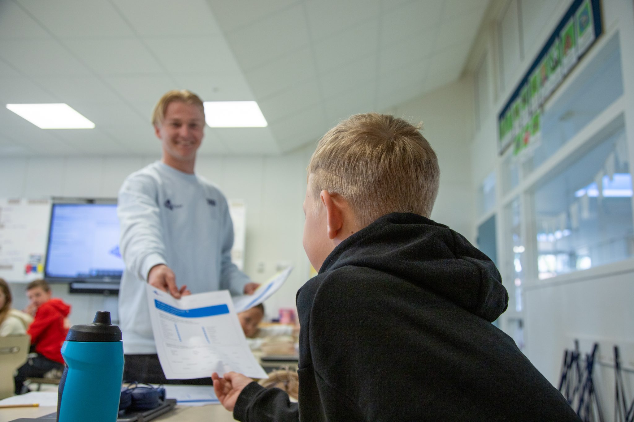 Een Digicoach geeft een werkblad aan een leerling tijdens een les digitale geletterdheid.