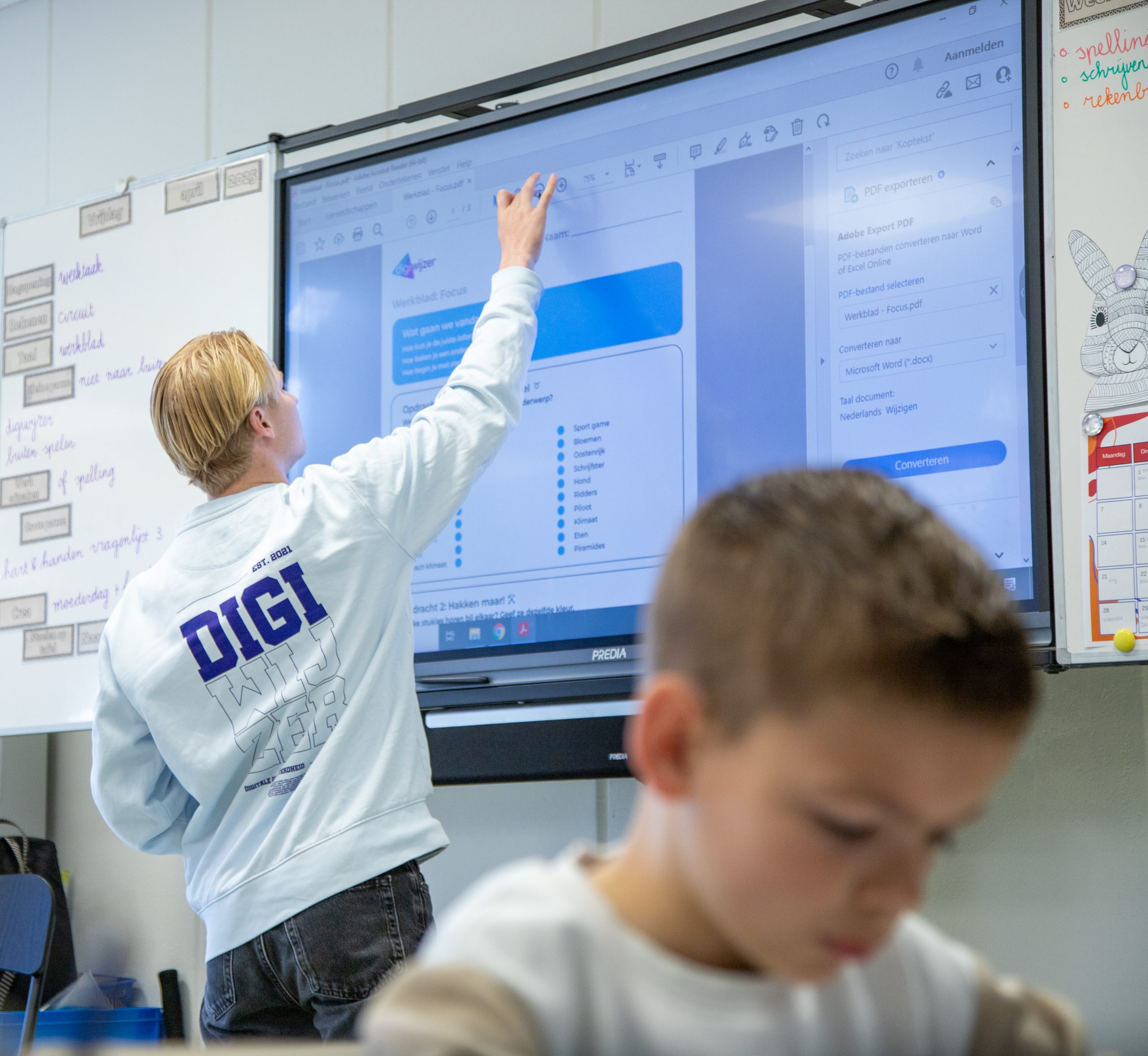 Een Digicoach geeft uitleg bij een digitaal werkblad op het digibord tijdens een les.