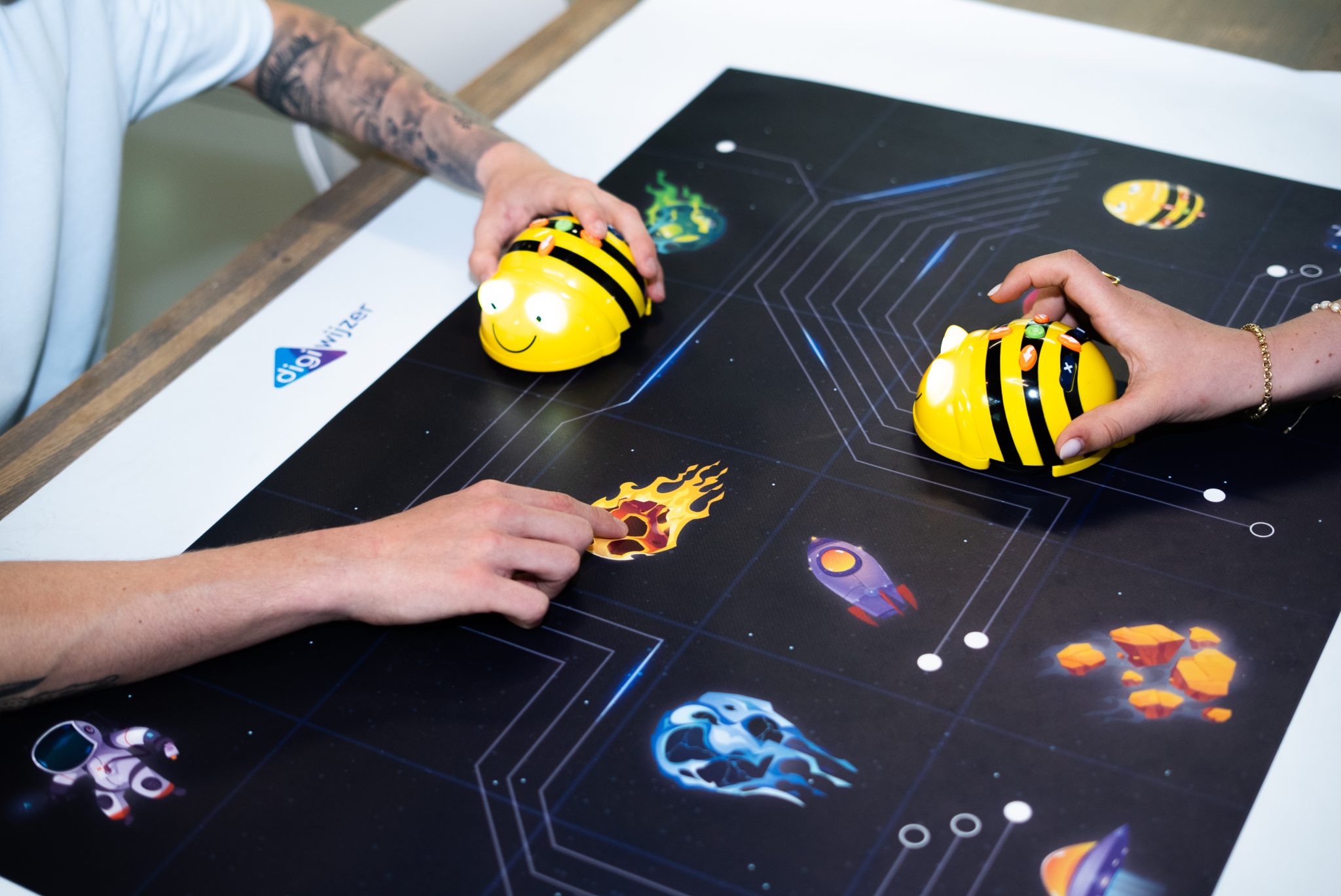 Twee personen programmeren Bee-Bots op een speelmat tijdens een les computational thinking.