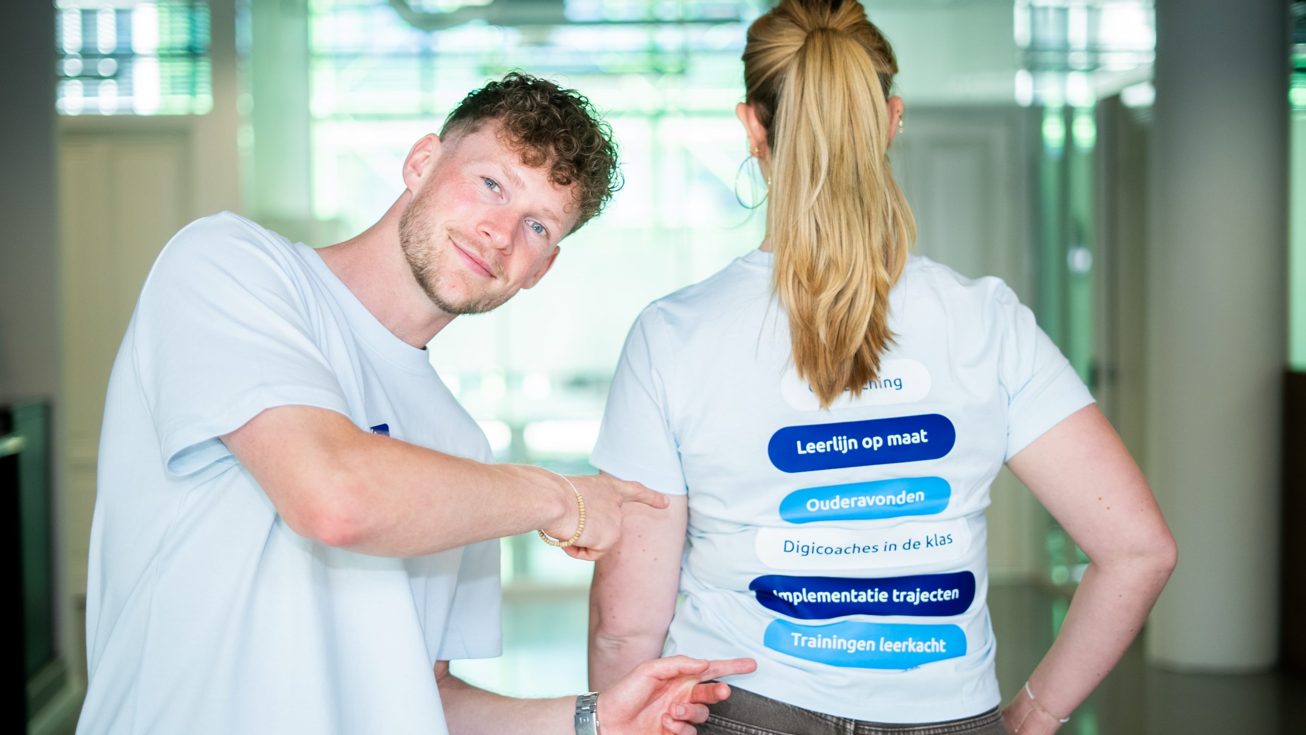 Digicoach wijst naar de verschillende onderwijsoplossingen op een Digiwijzer-shirt.