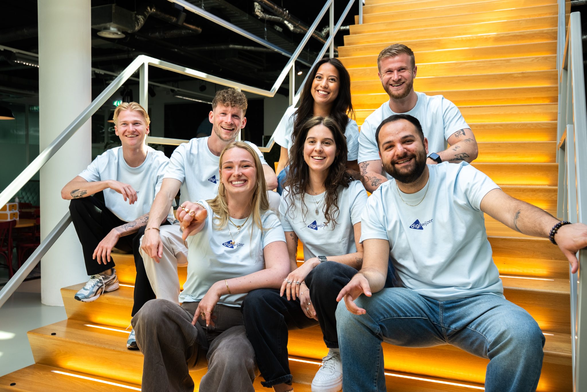 Team van Digiwijzer poseert op een trap en ondersteunt basisscholen bij digitale geletterdheid in het primair onderwijs.