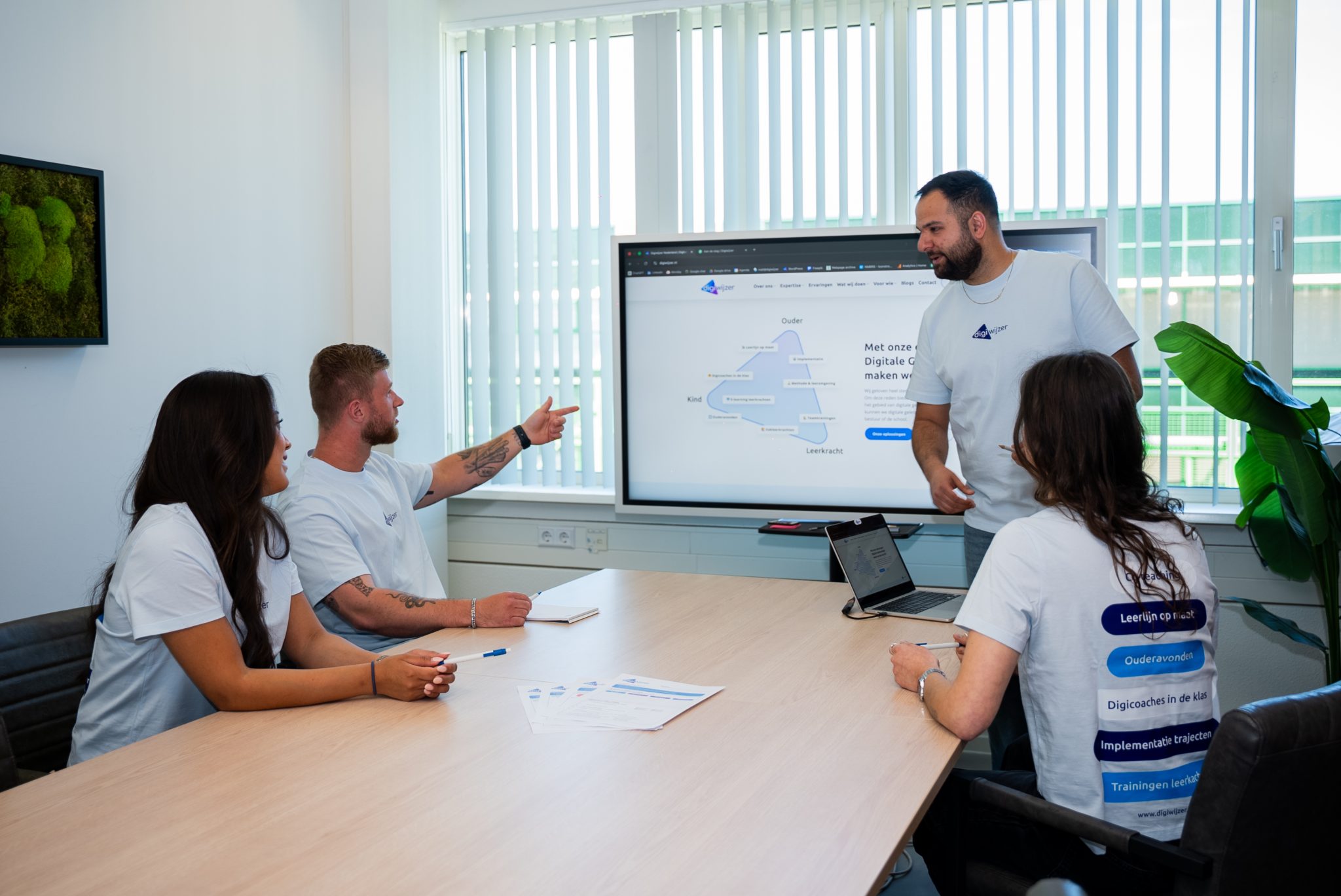 Digiwijzer-team bespreekt een implementatie van digitale geletterdheid tijdens een overleg met een interactief scherm waarop de Digiwijzer-aanpak wordt toegelicht.