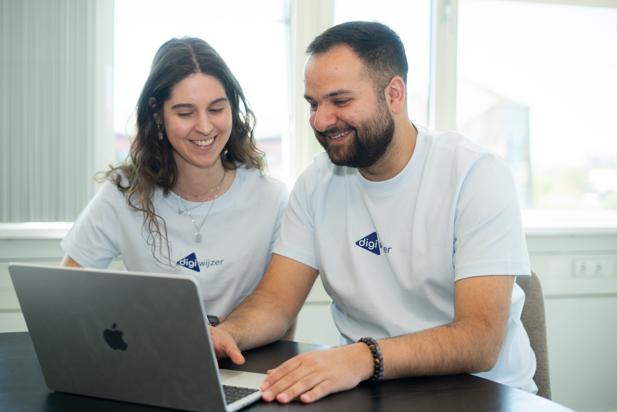 Een Digiwijzer-medewerker en een leerkracht bekijken samen een laptop tijdens de voorbereiding van een les digitale geletterdheid.