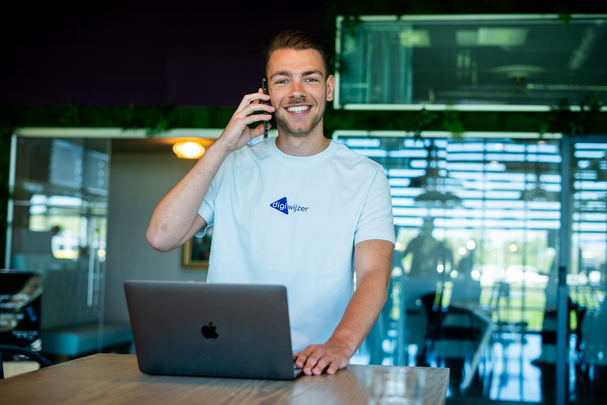 Medewerker van Digiwijzer staat achter een laptop en voert een telefonisch overleg op kantoor.