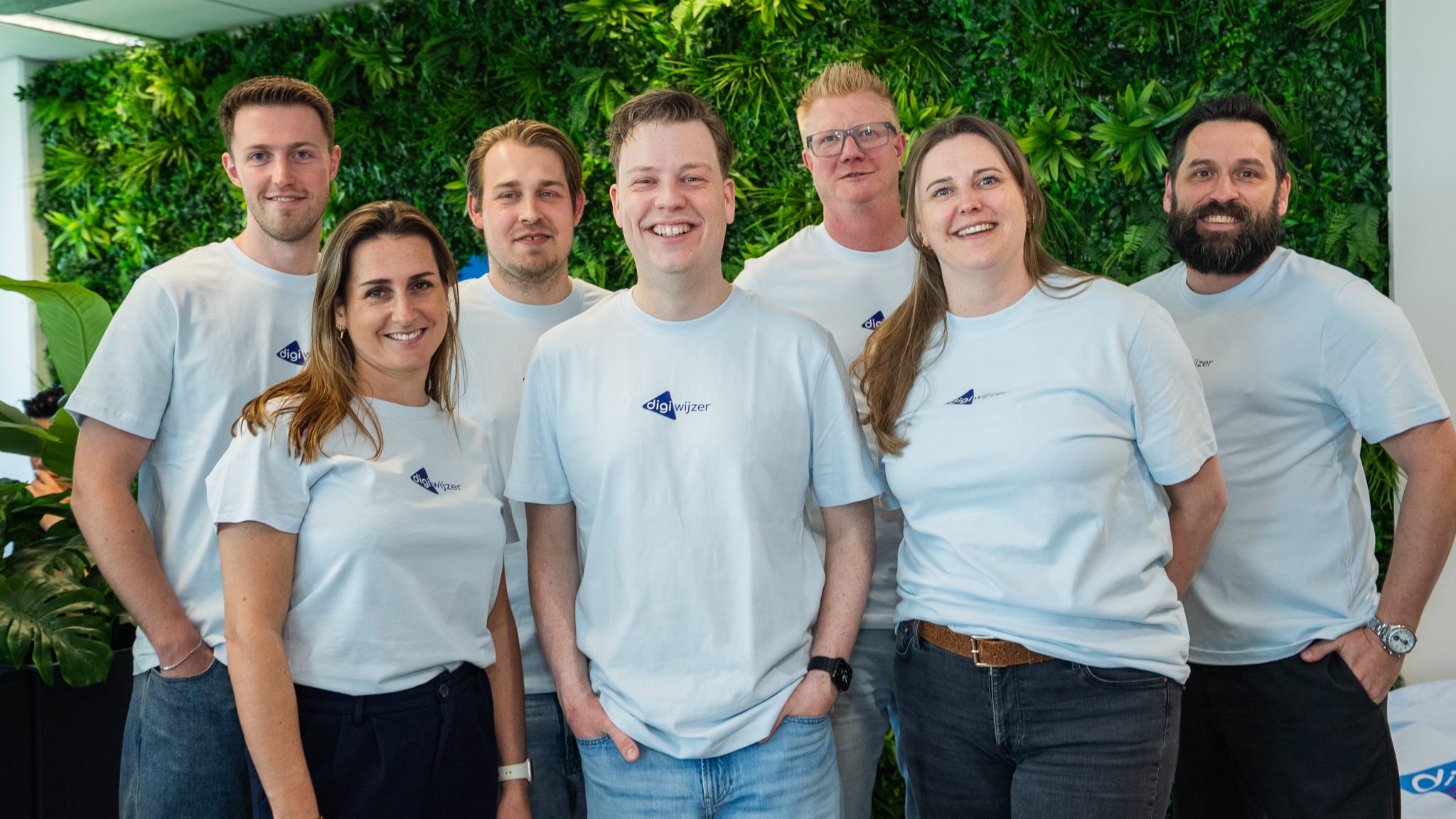 Een groep medewerkers van Digiwijzer poseert samen voor een groene plantenwand.