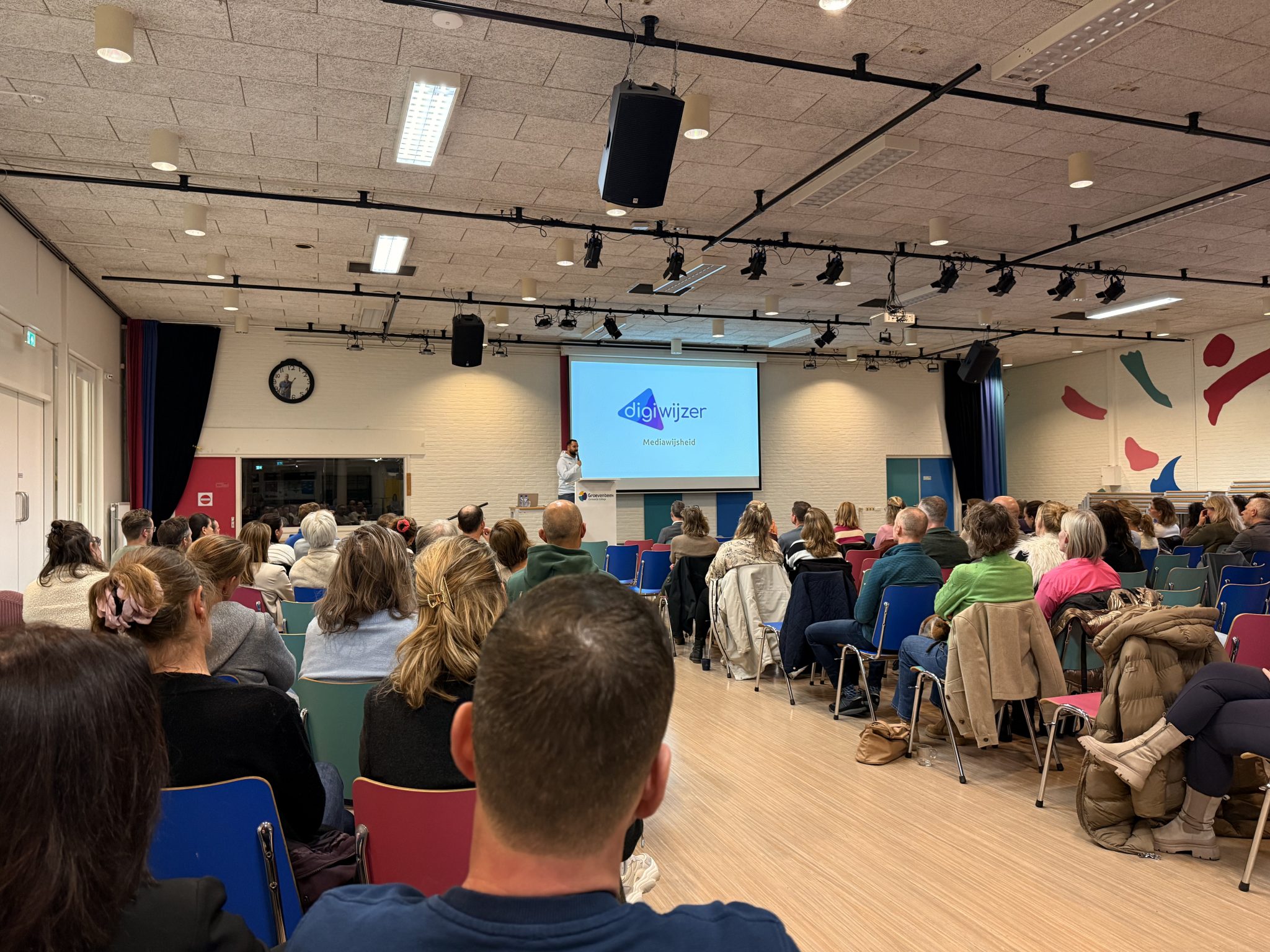 Ouderavond van Digiwijzer over mediawijsheid waarbij ouders in een volle zaal luisteren naar een presentatie over digitale geletterdheid.