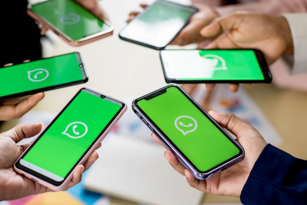 Meerdere kinderen houden een smartphone met het WhatsApp-logo vast, wat de vele groepsapps en chats tussen jongeren symboliseert.