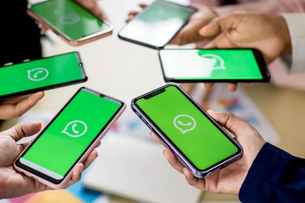 Meerdere kinderen houden een smartphone met het WhatsApp-logo vast, wat de vele groepsapps en chats tussen jongeren symboliseert.